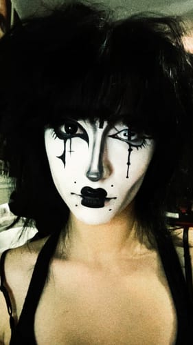 Reviewer with theatrical makeup showcasing one Halloween black block contact lens for a costume look.