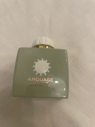 Cliente mostra il flacone di profumo Existence di Amouage su una superficie bianca.