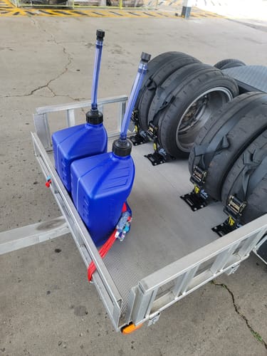 Customer's two blue 5 Gallon Jugs secured in a utility trailer with long spouts, next to several tires.