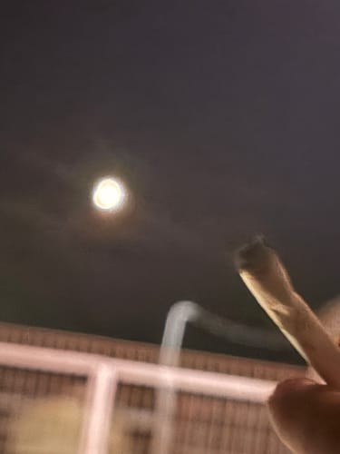 Partial view: Reviewer's hand holding a lit, hand-rolled Montgomery Benz THCA Flower cigarette against a night sky.