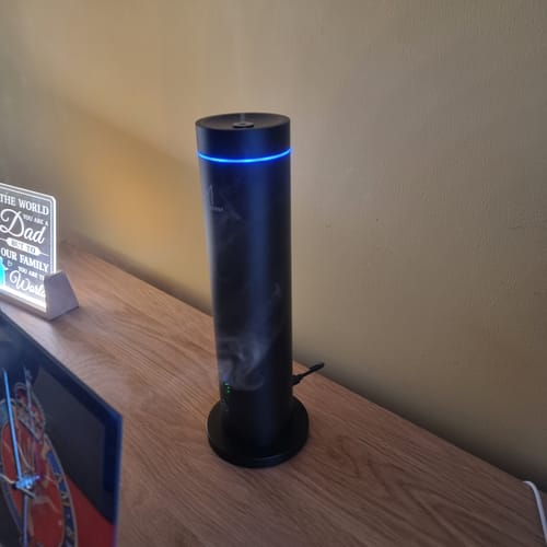 Customer's black NovaMist diffuser on a wooden surface, showing its blue ambient light while releasing a wisp of mist.
