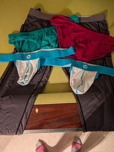 Reviewer displays items from their Mega Value Mystery Pack, including colorful briefs, jockstraps, and dark leggings on a bed.