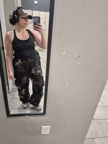 Reviewer taking a mirror selfie in a gym wearing the baggy Heritage Camo Cargo Sweats.