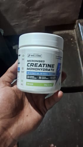 Reviewer holding the white tub of Wellcore Pure Micronised Creatine Monohydrate in Kiwi Kick flavor.