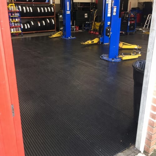 Customer's black flat ribbed rubber flooring installed in a garage workshop with two blue car lifts.