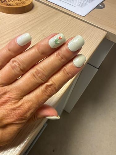Eine Kundin zeigt ihre salbeigrünen Mystic Sage UV Gelfolien. Ein Nagel ist als Akzent mit einer kleinen Blume verziert.