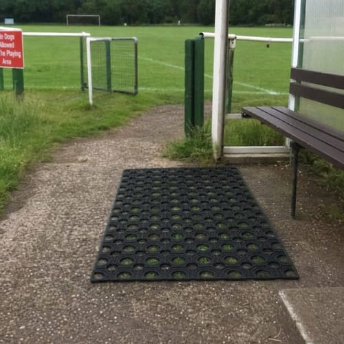 Reviewer's sturdy rubber grass mat on a path next to a bench at a sports field.