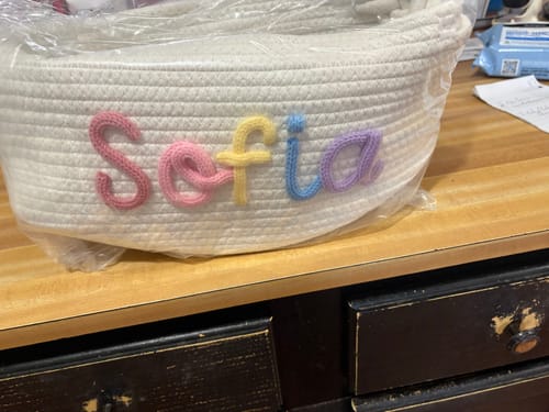 Customer's personalized knitted basket with the name 'Sofia' in colorful yarn, shown new in its packaging.
