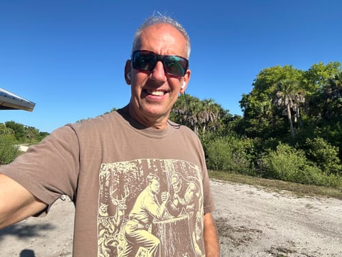 Customer wearing the brown graphic t-shirt outdoors, smiling for a selfie.
