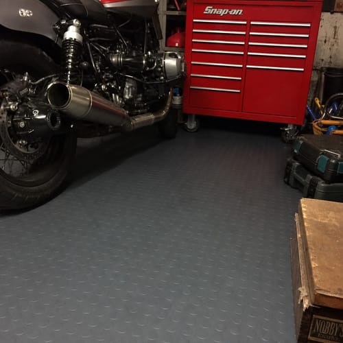 Reviewer's grey Studded Dot Penny Rubber Flooring installed in a garage under a motorcycle and tool chest.