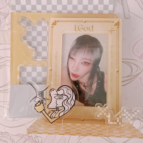 Reviewer's XLOV 'I,God' official MD set, featuring a beige photocard frame and a clear acrylic stand on a checkered base.