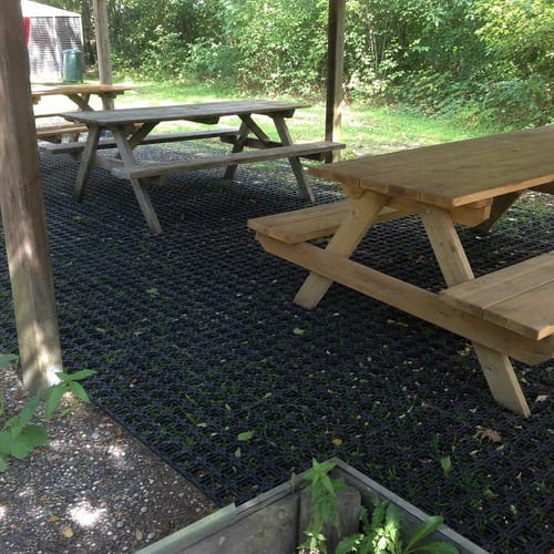 Customer's black Rubber Grass Mats installed under wooden picnic tables in a grassy, outdoor seating area.