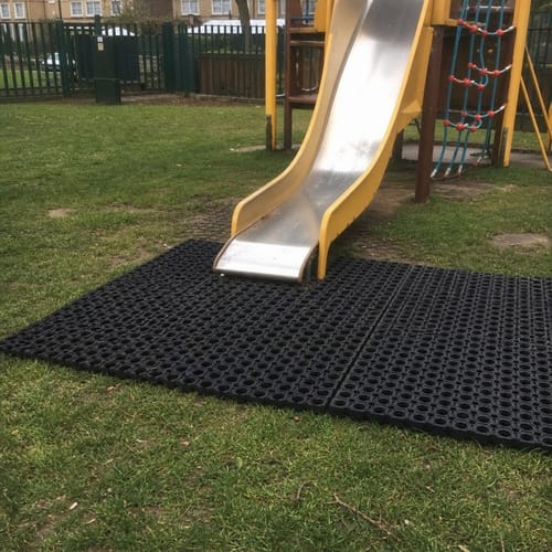 Customer's black rubber grass mats placed on grass at the bottom of a playground slide to prevent mud.
