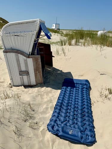 Kundenfoto der aufgeblasenen, blauen Isomatte an einem Sandstrand neben einem Strandkorb.