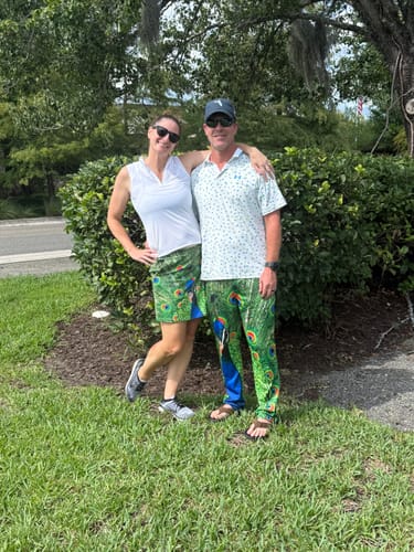 Customer wearing the peacock golf skirt, posing with a person in matching peacock pants outdoors.