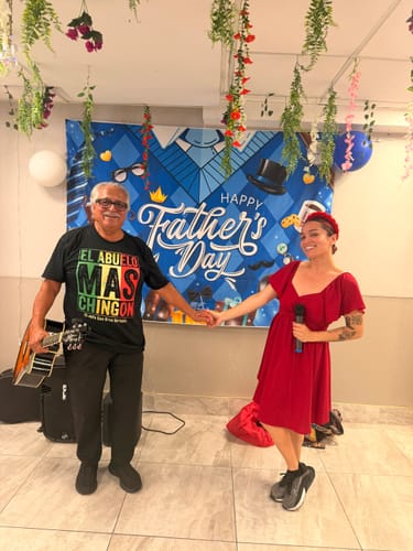 Customer wearing the black El Abuelo Mas Chingon T-Shirt, holding a guitar next to a person at a Father's Day event.