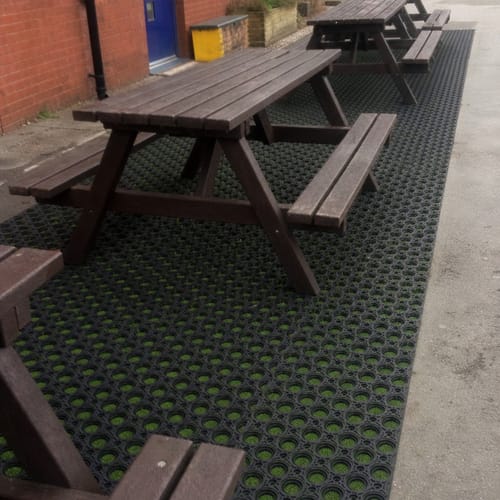 Customer's black Rubber Grass Mats installed under picnic tables in a schoolyard, allowing grass to grow through.