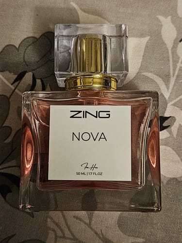 Reviewer's NOVA perfume bottle with a clear cap and gold details on a patterned surface.