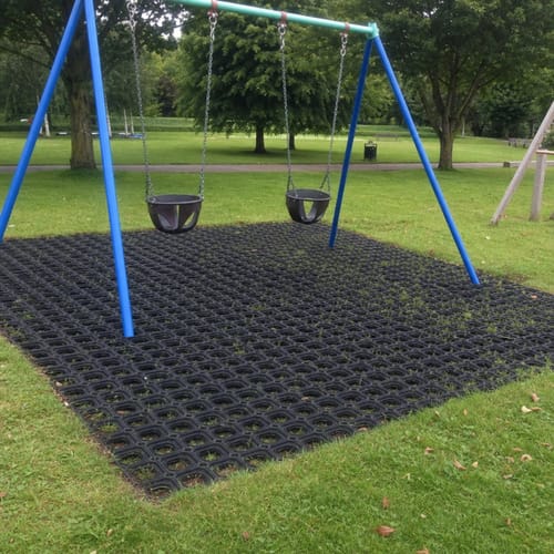 Customer's Rubber Grass Mats installed under a swing set, with grass growing through the holes.