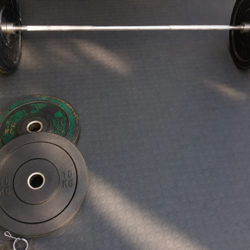 Customer's photo of the grey Studded Dot Rubber Flooring installed in a gym, with a barbell and weights on it.