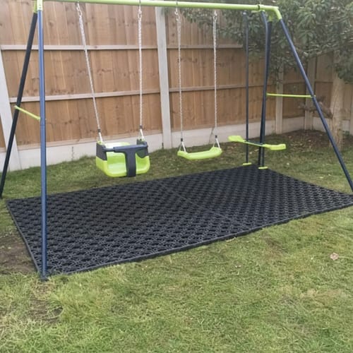 Customer's rubber grass mats installed under a children's swing set on a lawn.
