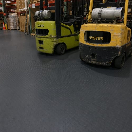 Customer's black Studded Dot Penny Rubber Flooring installed in a warehouse with two yellow forklifts parked on its durable surface.