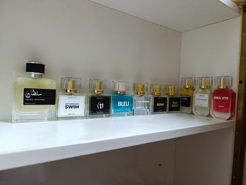 Customer's collection of various perfume bottles with clear and blue liquids arranged on a white shelf.