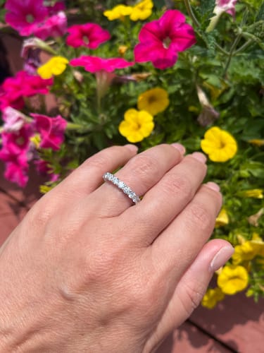 Customer's hand wearing the platinum customization wedding band with round diamonds in front of bright flowers.