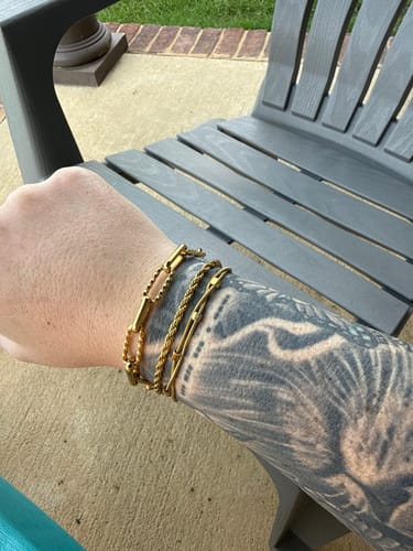 Customer's tattooed arm showing several gold bracelets stacked on the wrist.