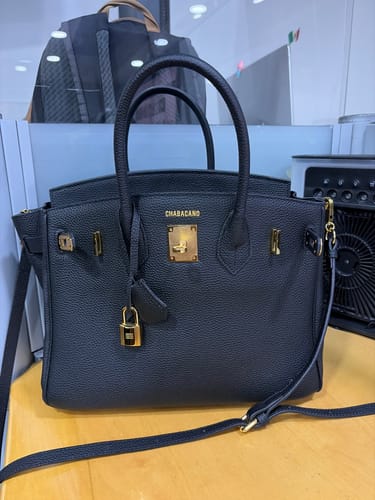 Cliente mostrando su bolso Carrie negro con elegantes herrajes dorados sobre un escritorio.