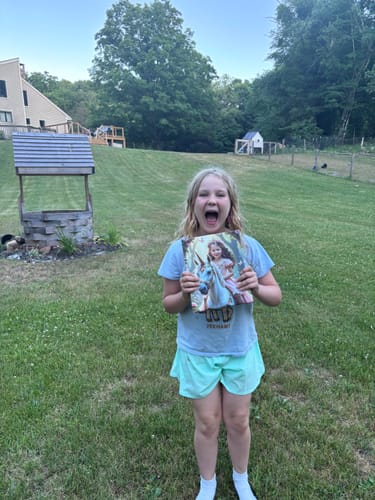 Customer with a joyful, excited expression holding The Enchanted Unicorn Princess product outdoors.