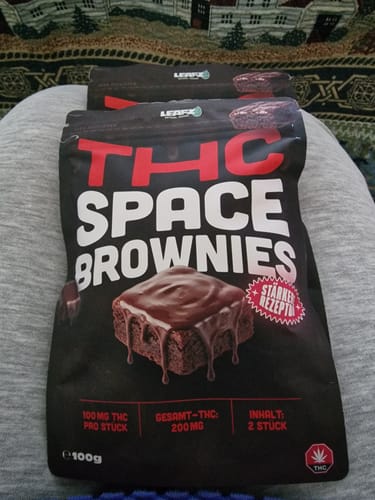 Ein Kunde zeigt zwei schwarze Packungen der THC Spacebrownies auf seinem Schoß.