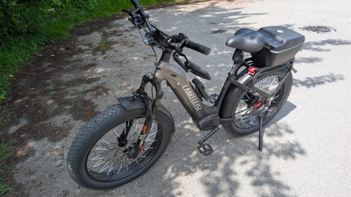 Reviewer's grey Lankeleisi MG600 Plus fat bike on a paved trail, showing a hard case added to the rear rack.