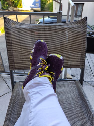 Rezensent trägt die lila Smart II Barfußschuhe mit gelben Schnürsenkeln und entspannt sich auf einem Stuhl.