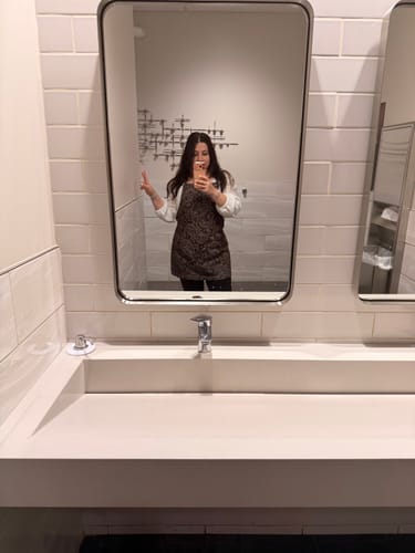 Reviewer taking a mirror selfie while wearing the patterned The Outlaw apron.