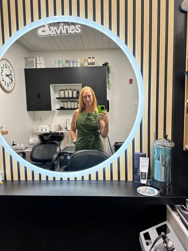Reviewer taking a mirror selfie wearing the Olive Green Apron in a salon.