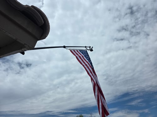 Customer's heavy duty American flag hanging from a pole mounted on a house under a cloudy sky.