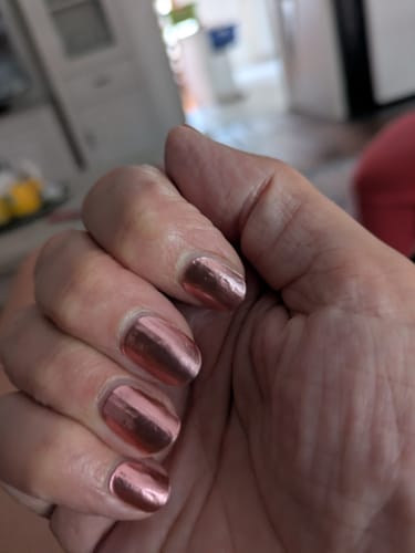 Nahaufnahme der Hand einer Kundin mit den aufgetragenen 'Rosé Chrome' UV-Nagelfolien, die einen starken, kupferfarbenen Glanz haben.