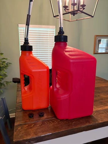 Customer's red 5-gallon and smaller orange Tuff Jugs with auto-stop spouts standing side-by-side on a wooden table.