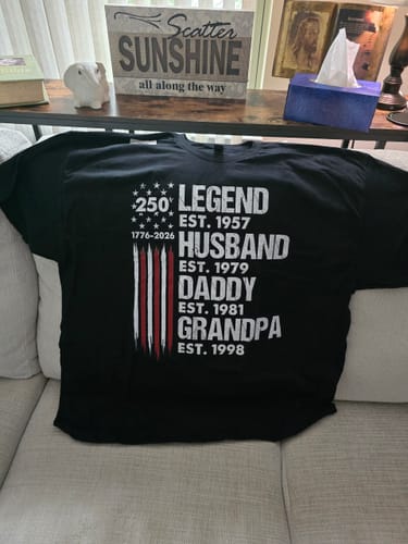 Customer's personalized black 'Proud Grandpa' shirt laid flat on a couch, displaying the patriotic 'Legend' text design.