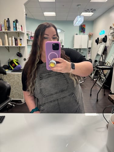 Customer takes a mirror selfie in a salon wearing the black acid washed bib apron.