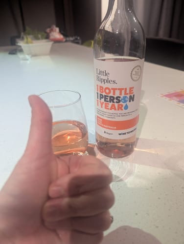 A reviewer's hand gives a thumbs-up next to a glass of Rosé and the bottle on a white countertop.