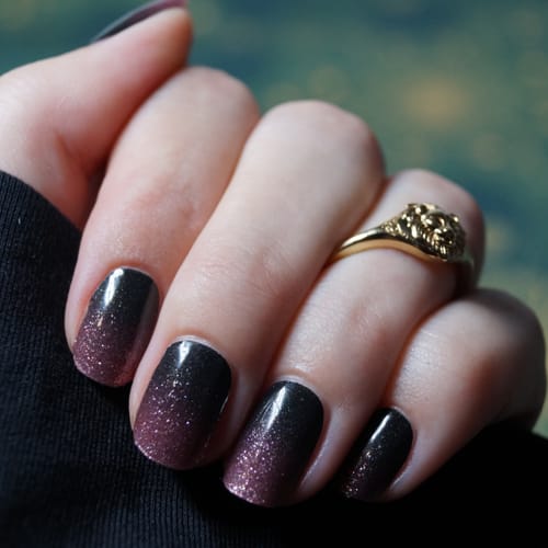 Hand einer Kundin, die die aufgetragenen 'Blush Nightfall' UV-Gel-Folien mit einem schwarz-rosa Glitzerverlauf zeigt.