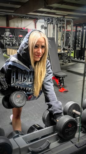 Reviewer wearing an oversized Yu-Gi-Oh!® Hoodie in a gym while picking up a dumbbell from a rack.