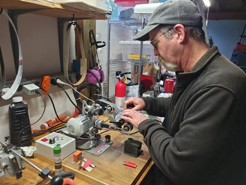 Reviewer using a Silicon Carbide Sanding Belt on a benchtop sander in a workshop.