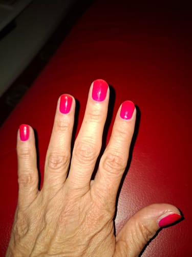 Hand einer Kundin, die die leuchtenden 'Hot Ombré' UV-Gel-Nägel mit einem Farbverlauf von Pink zu Rot trägt.