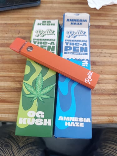 Customer's orange ROLLZ THCA Vape pen resting on the "OG Kush" and "Amnesia Haze" product boxes.