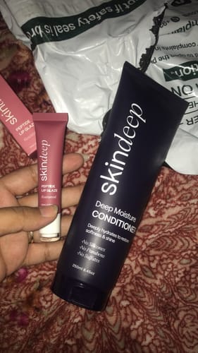 Reviewer holding the pink tube of Peptide Lip Glaze next to a larger bottle of Skindleep conditioner.