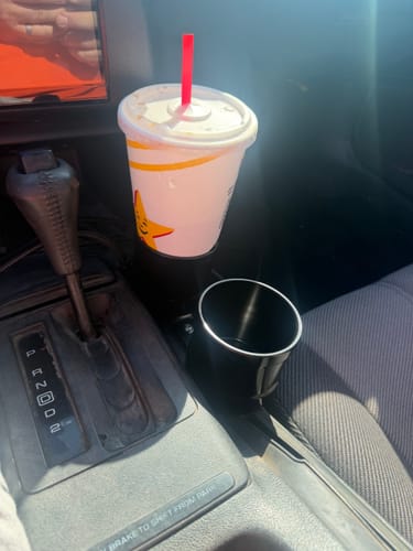 Reviewer's black Dual Billet Cup Holder installed in a car's center console, with one holder empty and the other holding a drink.