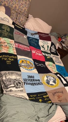 Customer's colorful Premium T Shirt Quilt, made from many different t-shirt squares, spread across a bed.